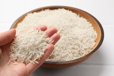 Photo of Woman holding raw basmati rice near bowl at white table, closeup