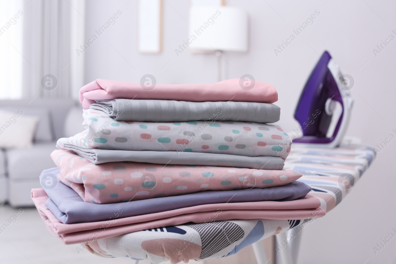 Photo of Stack of clean bed linens on ironing board in room