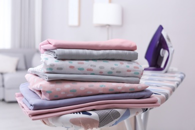 Photo of Stack of clean bed linens on ironing board in room
