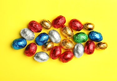 Chocolate eggs wrapped in colorful foil on yellow background, flat lay