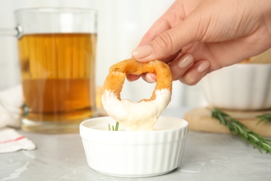 Photo of Woman dipping crunchy fried onion ring in sauce at grey marble table, closeup