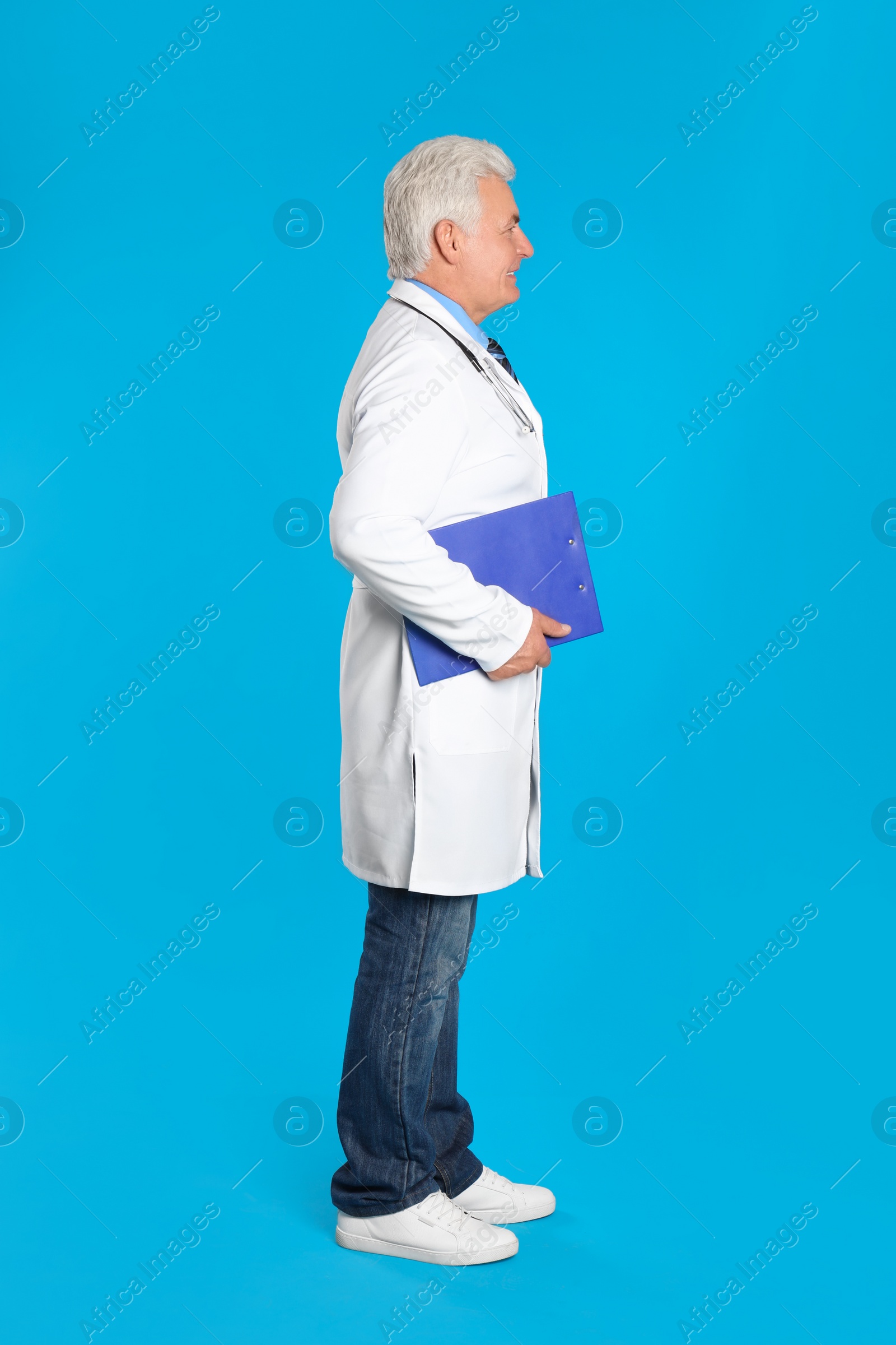 Photo of Senior doctor with clipboard on light blue background