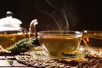 Photo of Cup of aromatic herbal tea and thyme on wooden table