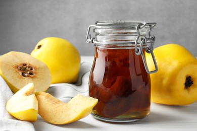 Photo of Tasty homemade quince jam in jar and fruits on white wooden table, closeup