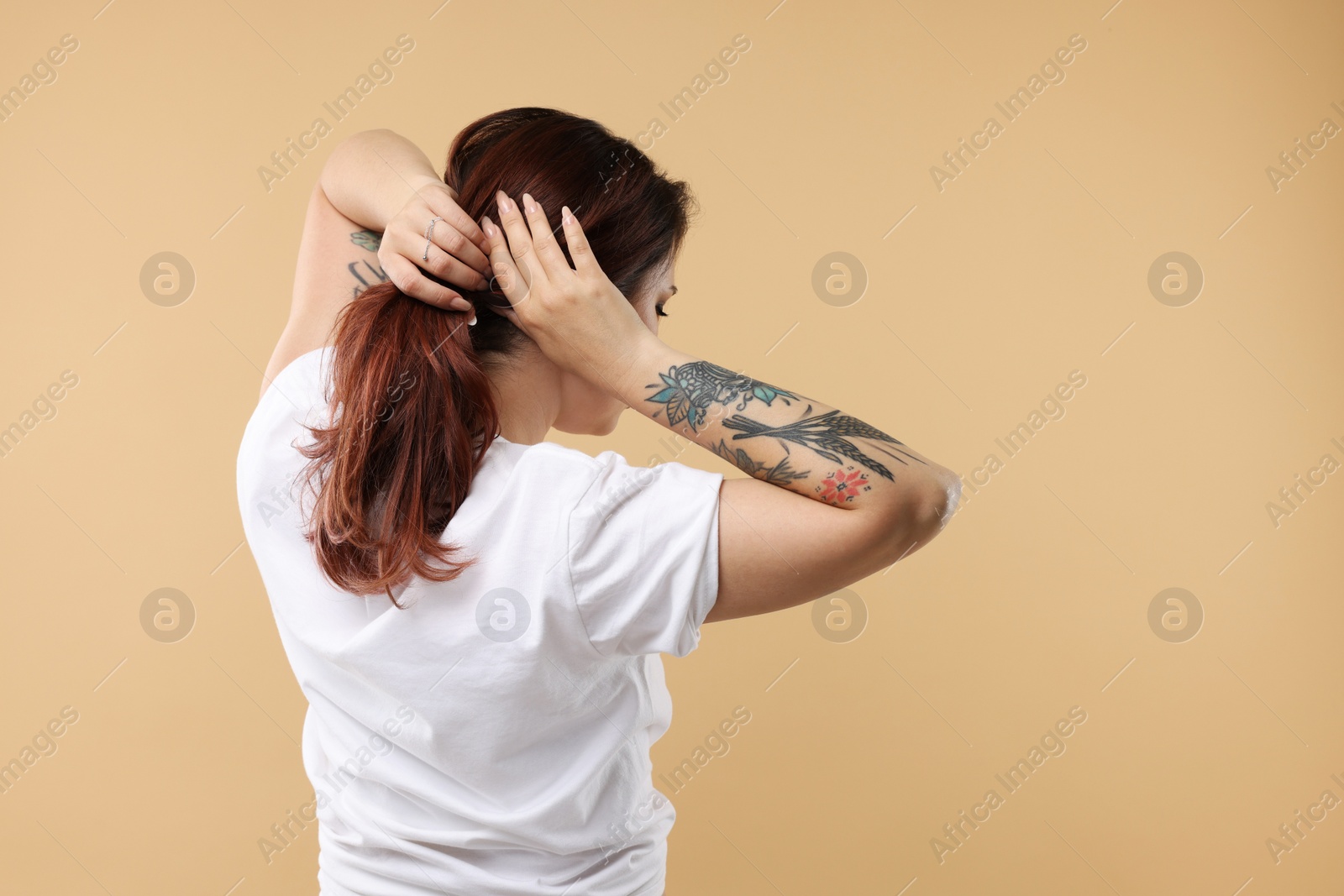 Photo of Stylish tattooed woman on beige background, back view. Space for text