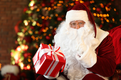 Photo of Santa Claus with gift box near Christmas tree indoors