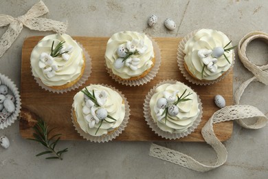 Photo of Tasty Easter cupcakes with vanilla cream, candies and ribbon on gray table, flat lay