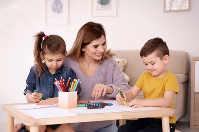 Photo of Cute little children and their nanny drawing at home