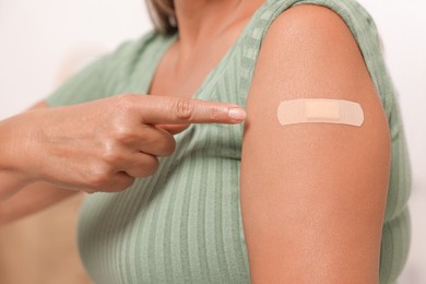Woman pointing at adhesive bandage after vaccination on blurred background, closeup