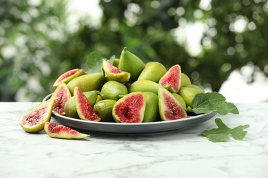 Cut and whole green figs on white marble table against blurred background
