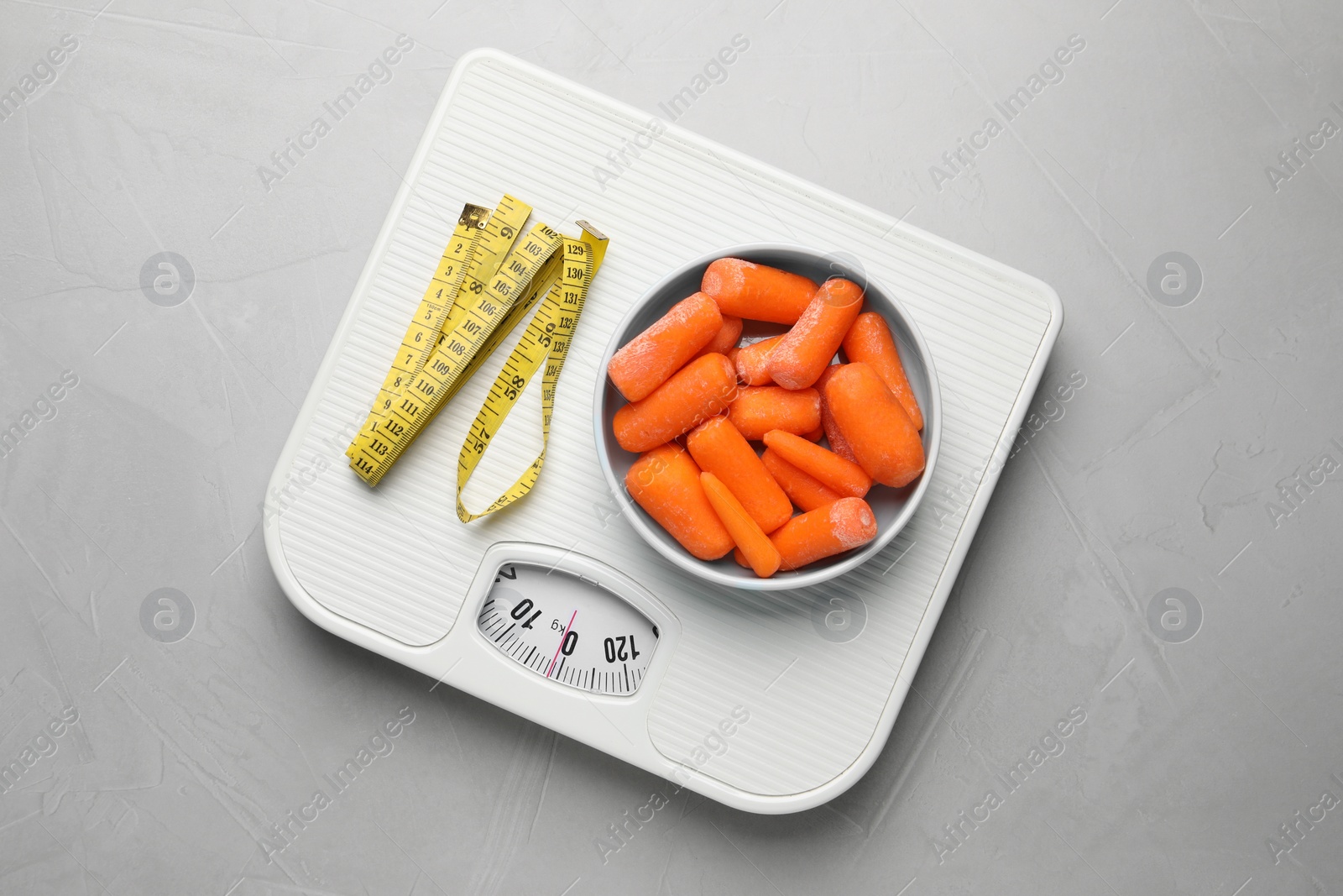 Photo of Healthy diet. Scale with carrots and measuring tape on light grey table, top view