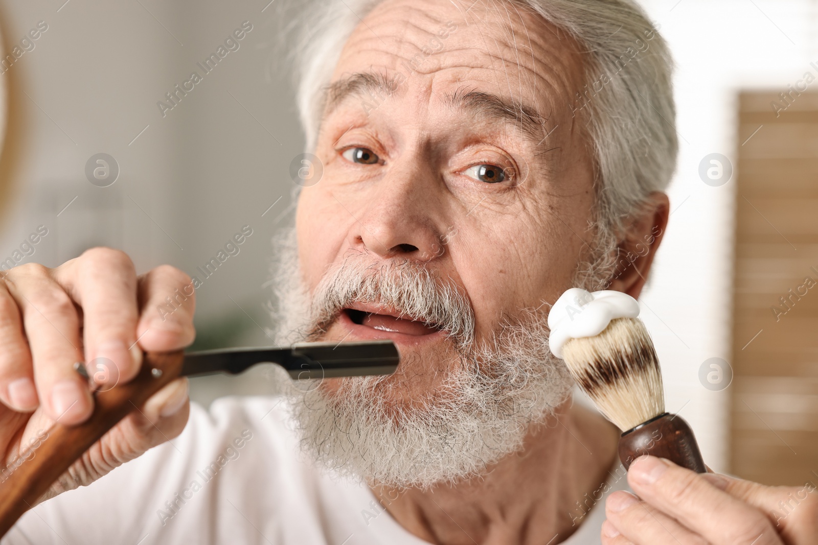 Photo of Man shaving mustache and beard with blade in bathroom