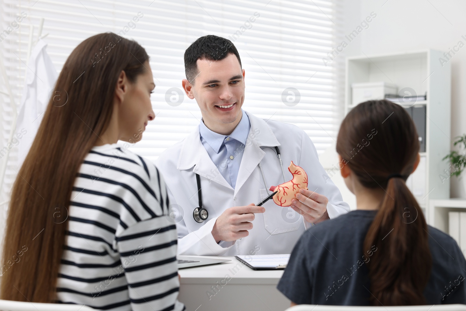 Photo of Gastroenterologist with model of stomach consulting woman and her daughter in clinic