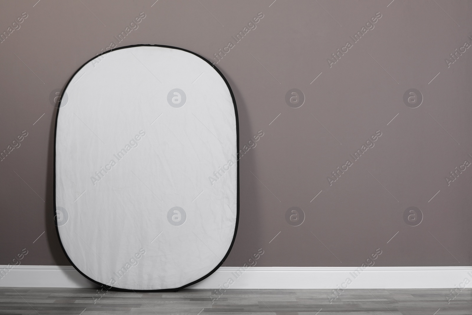 Photo of Professional light reflector near grey wall in room, space for text. Photography equipment