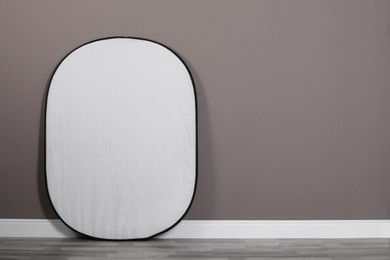 Photo of Professional light reflector near grey wall in room, space for text. Photography equipment