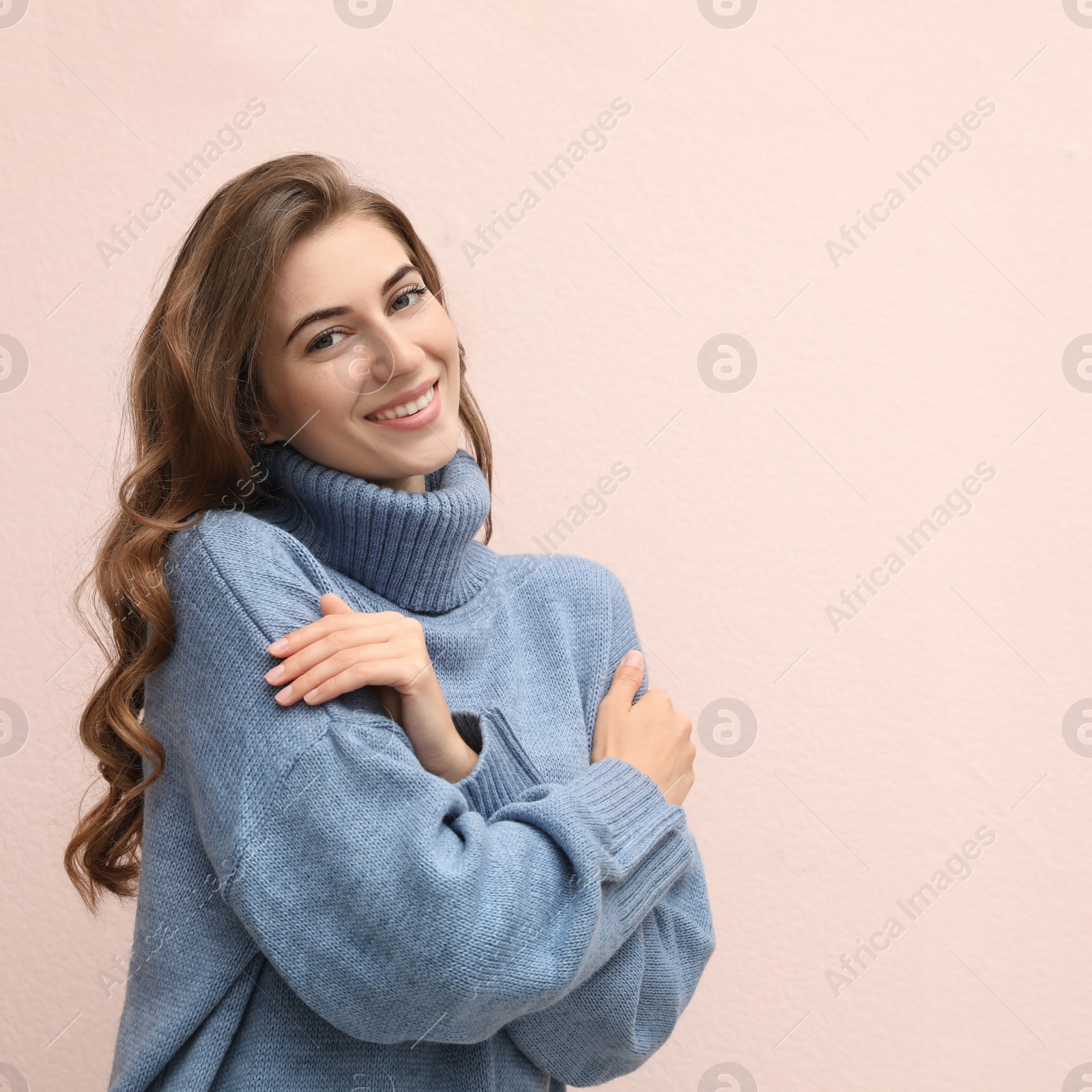 Photo of Beautiful young woman wearing warm blue sweater on light pink background. Space for text