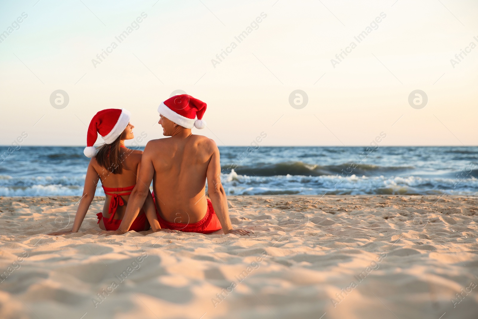 Photo of Lovely couple with Santa hats together on beach, back view. Christmas vacation