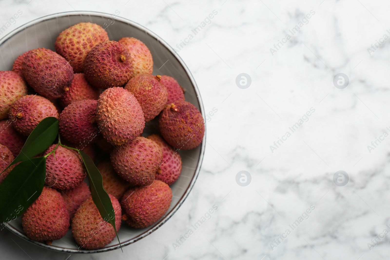 Photo of Fresh ripe lychee fruits in bowl on white marble table, top view. Space for text