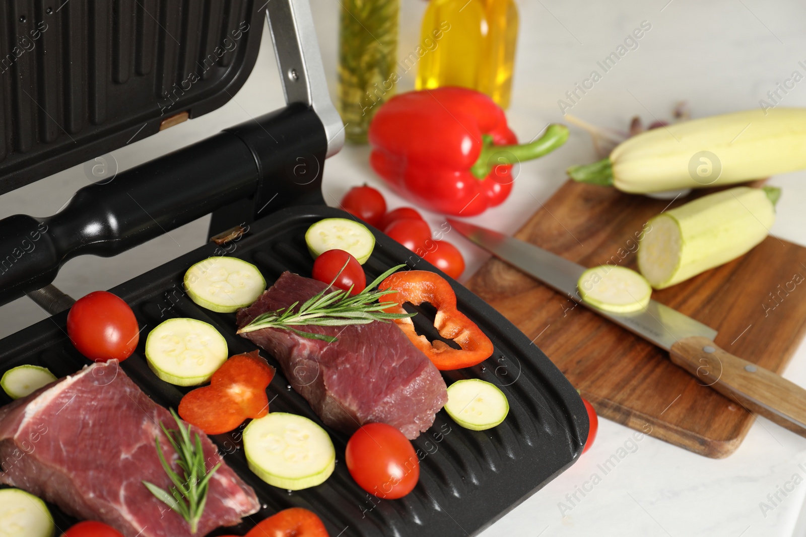 Photo of Electric grill and different products on white wooden table, closeup