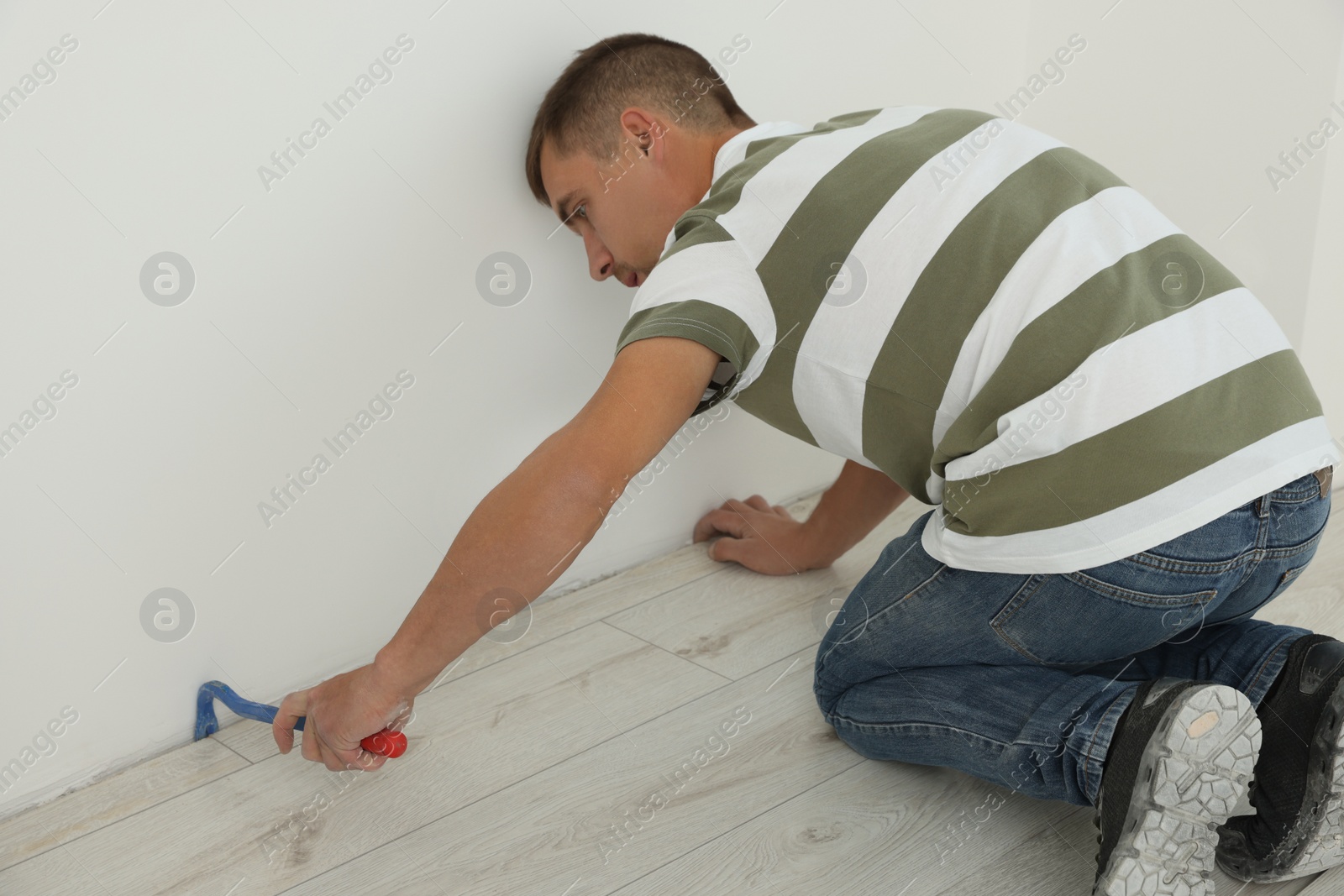 Photo of Professional worker using nail puller during installation of new laminate flooring indoors