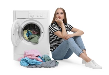 Upset woman with dirty clothes near washing machine on white background