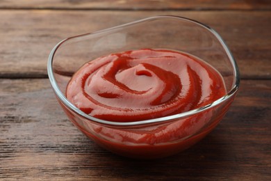 Bowl of tasty ketchup on wooden table, closeup