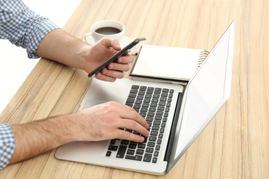 Man with mobile phone and modern laptop at wooden table, closeup