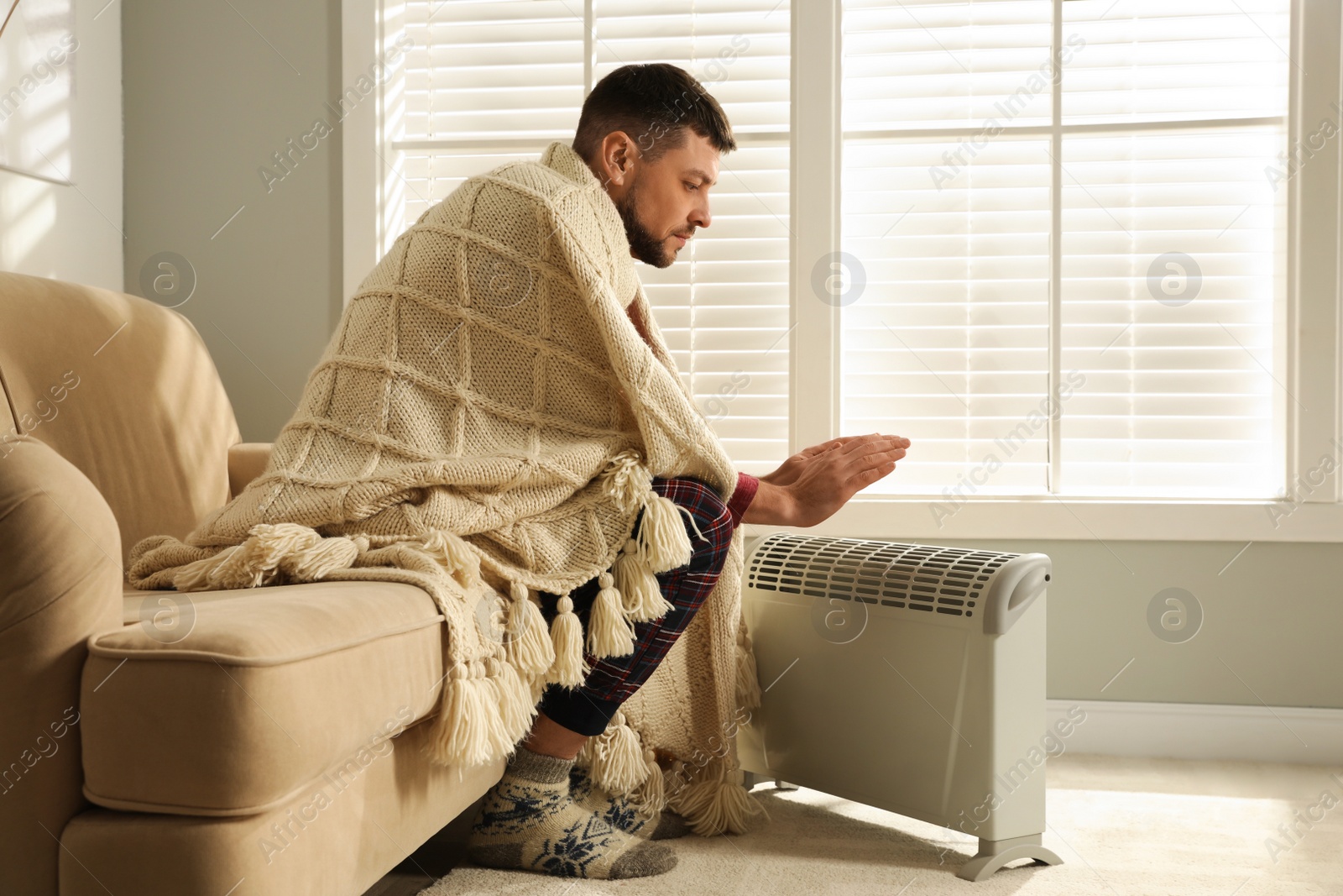 Photo of Man warming hands near electric heater at home