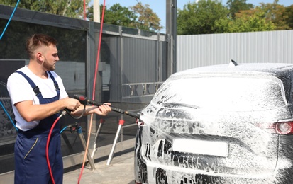 Photo of Young worker cleaning automobile with high pressure water jet at car wash