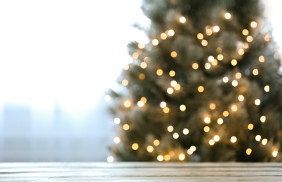 Photo of Blurred view of beautiful Christmas tree with yellow lights near window indoors, focus on wooden table. Space for text