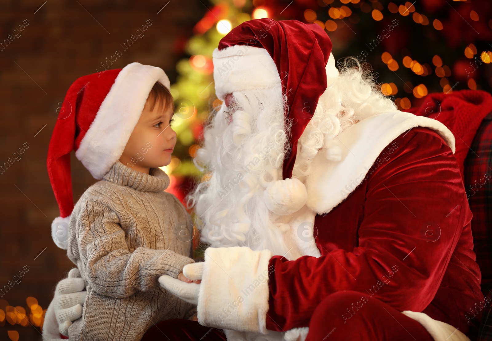 Photo of Santa Claus and little boy near Christmas tree indoors