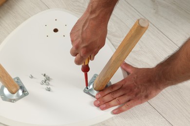Man with screwdriver assembling stool on floor, above view