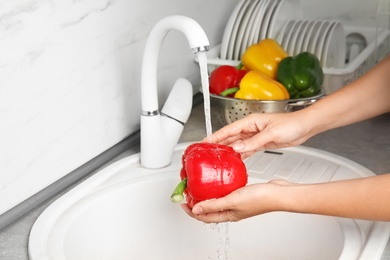 Photo of Woman washing paprika pepper in kitchen sink, closeup