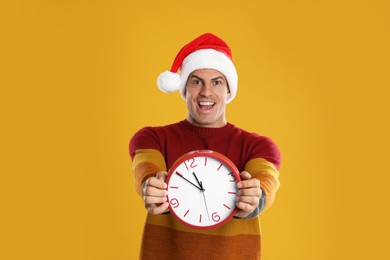 Photo of Man in Santa hat with clock on yellow background. New Year countdown