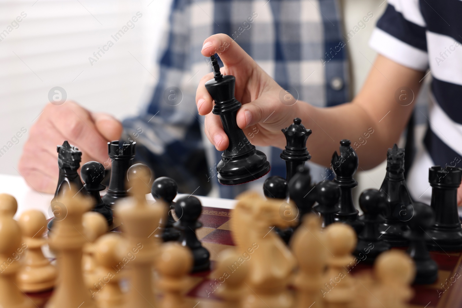 Photo of Senior man teaching his grandson to play chess indoors, closeup