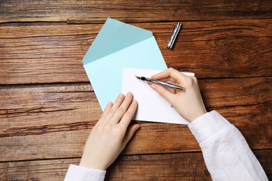 Woman writing letter at wooden table, top view