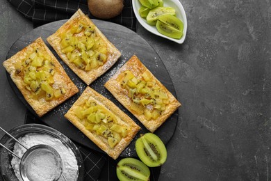 Photo of Fresh tasty puff pastry with sugar powder and kiwi served on grey table, flat lay. Space for text