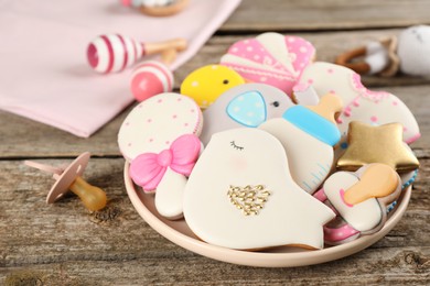 Photo of Cute tasty cookies of different shapes, pacifier and toys on wooden table, closeup. Baby shower party