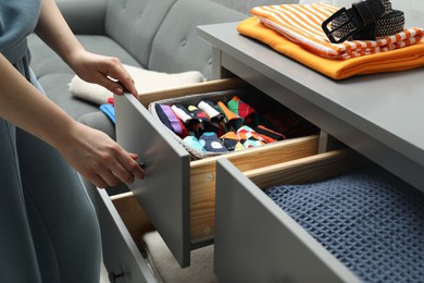 Photo of Woman opening drawer with different folded clothes indoors, closeup