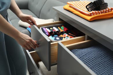 Woman opening drawer with different folded clothes indoors, closeup