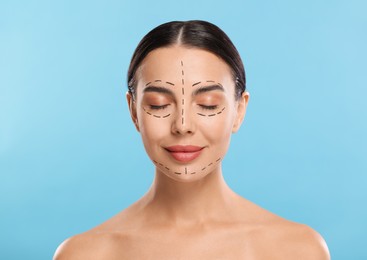 Photo of Young woman with marks on face for cosmetic surgery operation against light blue background