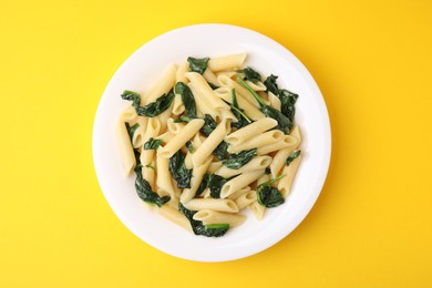 Tasty pasta with spinach and sauce on yellow table, top view