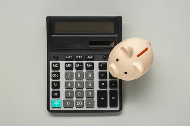 Calculator and piggy bank on light grey background, top view