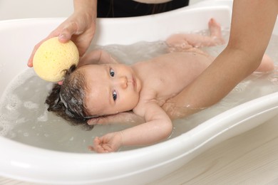 Photo of Mother bathing her little baby with sponge in bathtub, closeup