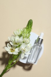 Bottle of cosmetic oil and flowers on beige background, top view