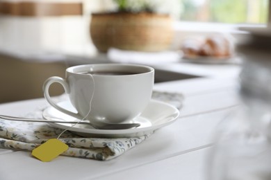Photo of Tea bag in cup on white wooden table indoors. Space for text