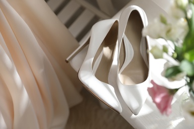 Photo of Pair of white high heel shoes, flowers and wedding dress indoors