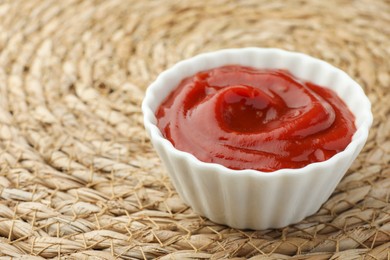 Bowl of tasty ketchup on wicker mat, closeup. Space for text