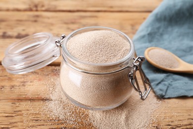 Photo of Glass jar and spoon with active dry yeast on wooden table, closeup