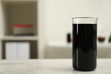 Beaker with black crude oil on light grey table, space for text
